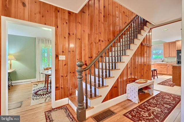 staircase featuring wood-type flooring, crown molding, a baseboard heating unit, and wooden walls