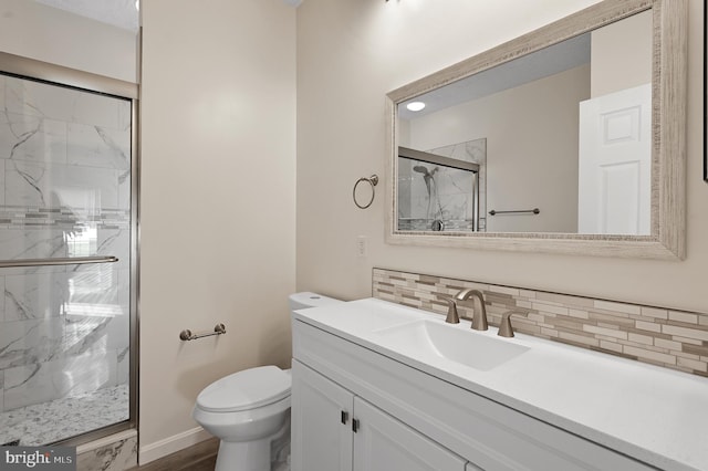 bathroom with vanity, toilet, a shower with shower door, and backsplash