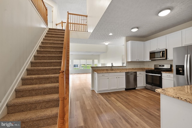 kitchen featuring appliances with stainless steel finishes, light hardwood / wood-style flooring, a textured ceiling, and white cabinets