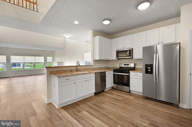 kitchen featuring white cabinets, kitchen peninsula, stainless steel appliances, and light wood-type flooring