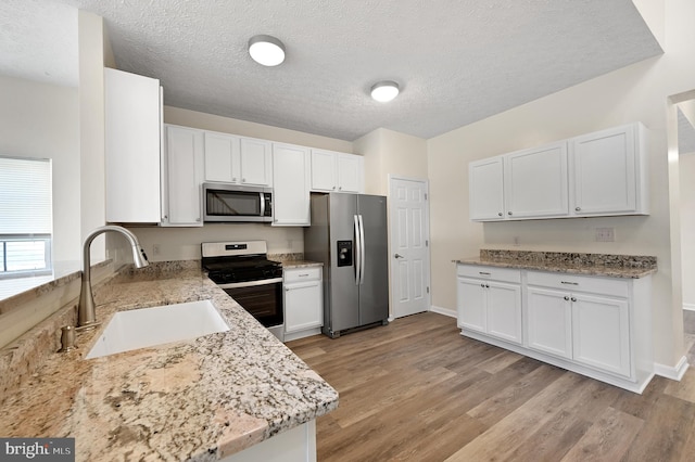 kitchen featuring light stone countertops, sink, white cabinetry, light hardwood / wood-style floors, and stainless steel appliances