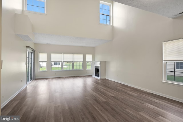 unfurnished living room with a towering ceiling, a textured ceiling, and dark wood-type flooring