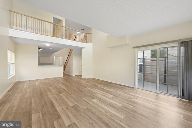 unfurnished living room featuring a textured ceiling, a towering ceiling, and light hardwood / wood-style flooring