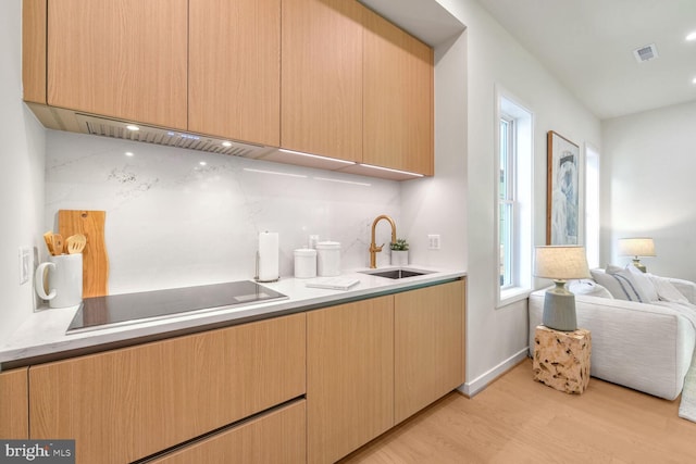 kitchen featuring light brown cabinetry, tasteful backsplash, black electric cooktop, sink, and light hardwood / wood-style flooring