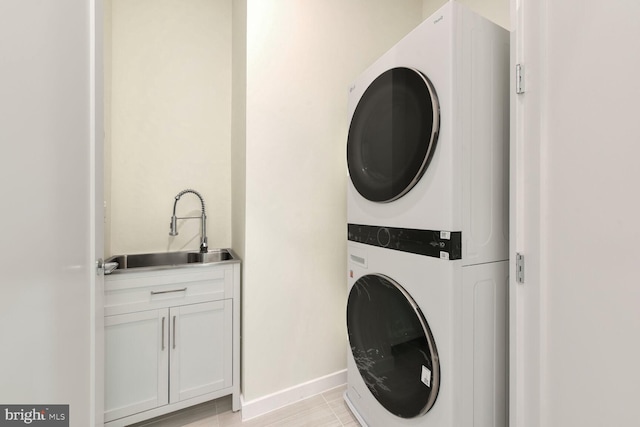 laundry area featuring cabinets, light tile patterned floors, stacked washer and dryer, and sink