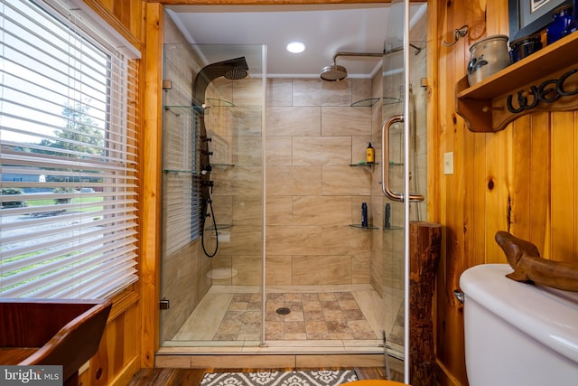 bathroom featuring a wealth of natural light, wooden walls, a shower with shower door, and toilet