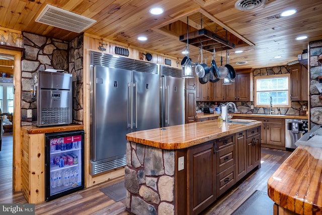 kitchen with wine cooler, dark hardwood / wood-style flooring, an island with sink, wooden ceiling, and stainless steel appliances