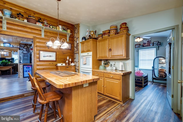 kitchen with wood counters, dark hardwood / wood-style flooring, a center island, pendant lighting, and log walls