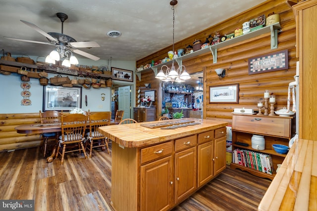 kitchen with dark hardwood / wood-style flooring, ceiling fan, pendant lighting, wooden counters, and rustic walls