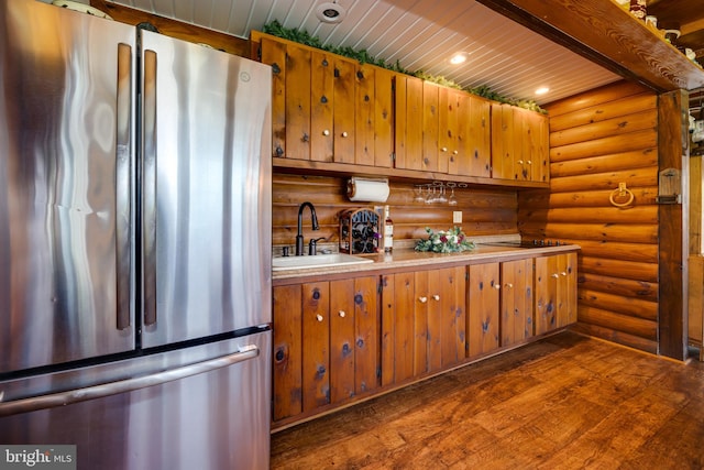 kitchen featuring black electric stovetop, sink, dark hardwood / wood-style flooring, log walls, and stainless steel refrigerator