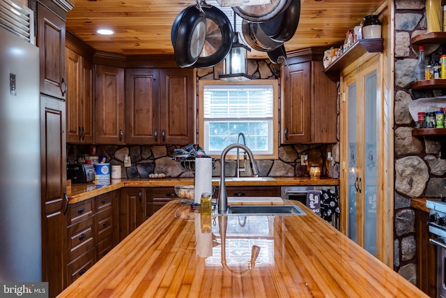 kitchen featuring dark brown cabinetry, sink, butcher block counters, and decorative backsplash