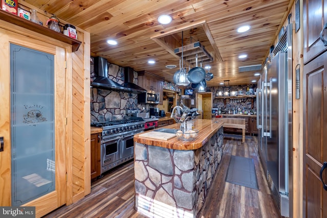 kitchen featuring premium appliances, wall chimney range hood, a center island, dark hardwood / wood-style flooring, and wooden counters