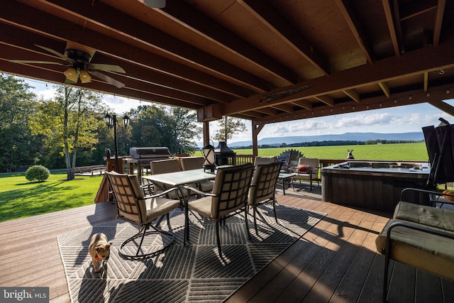 deck featuring a hot tub, grilling area, ceiling fan, a mountain view, and a lawn