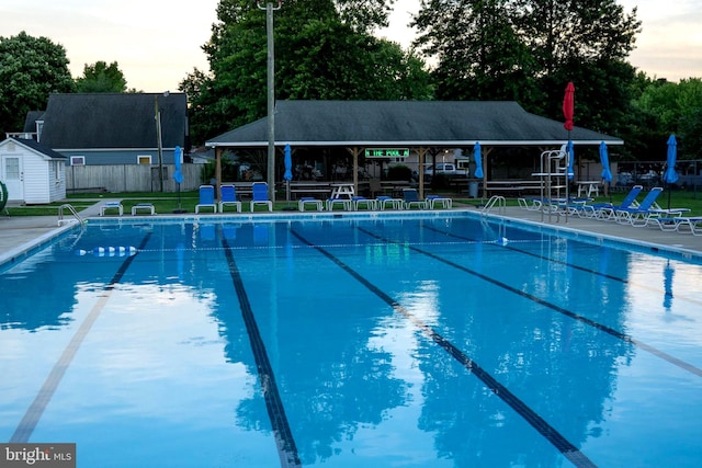 pool at dusk featuring a patio, a storage unit, and a gazebo