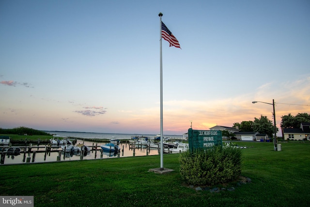 surrounding community with a water view, a boat dock, and a lawn