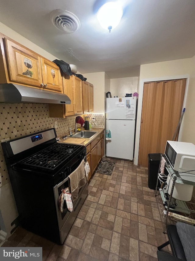 kitchen with gas stove, decorative backsplash, sink, and white refrigerator