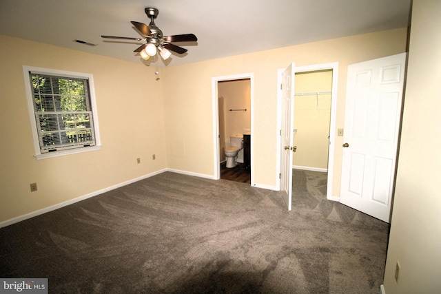 unfurnished bedroom with a walk in closet, ceiling fan, dark colored carpet, connected bathroom, and a closet