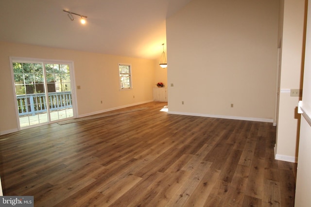 unfurnished living room featuring dark wood-type flooring, track lighting, baseboards, and lofted ceiling