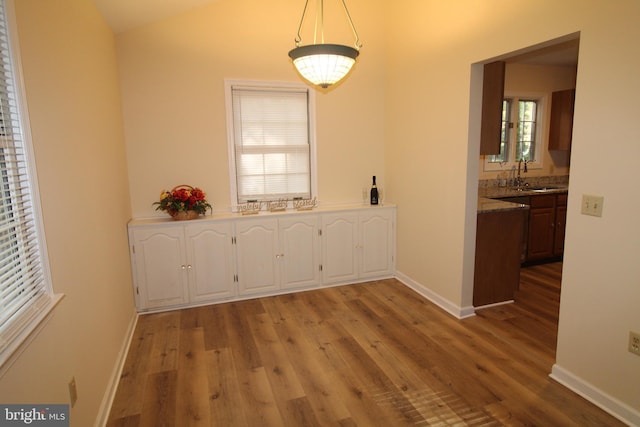 unfurnished dining area featuring light wood-style flooring, a sink, and baseboards