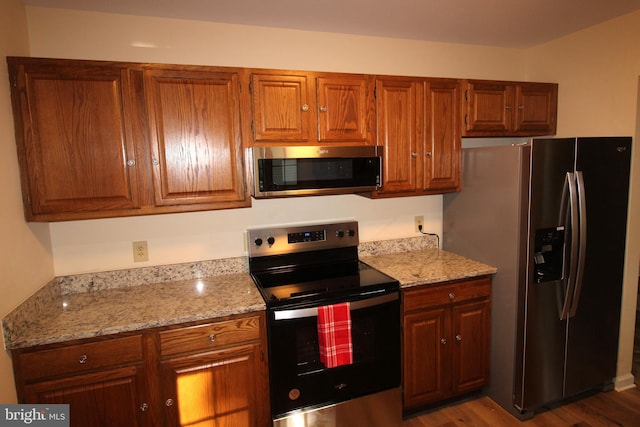 kitchen featuring stainless steel appliances, light stone countertops, brown cabinetry, and wood finished floors