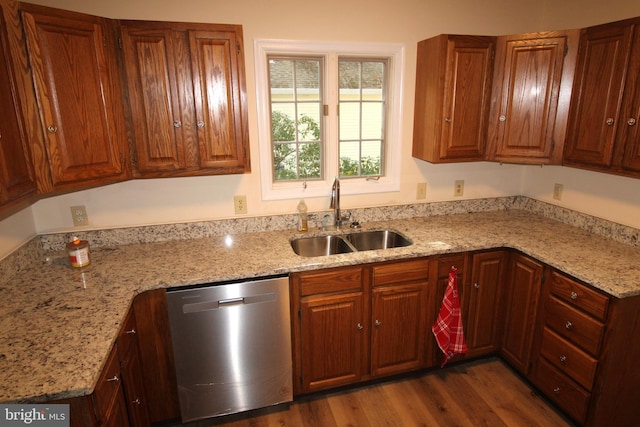 kitchen featuring a sink, brown cabinetry, wood finished floors, stainless steel dishwasher, and light stone counters