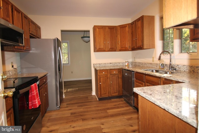 kitchen with a sink, dark wood-style floors, brown cabinetry, stainless steel appliances, and light stone counters
