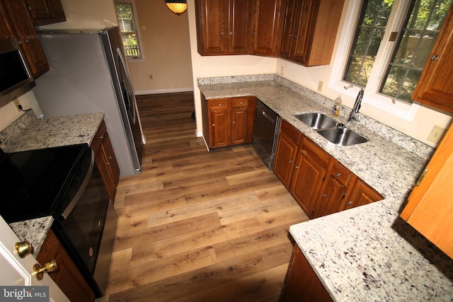 kitchen with light stone countertops, sink, black appliances, and light wood-type flooring