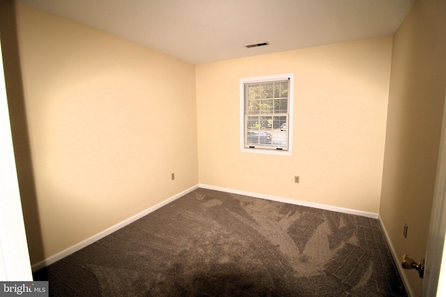 empty room featuring baseboards, dark colored carpet, and visible vents