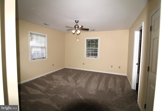 unfurnished room with dark carpet, visible vents, ceiling fan, and plenty of natural light