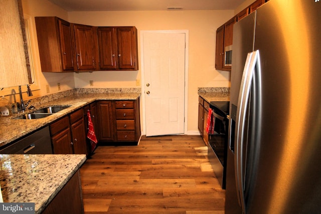 kitchen with light stone countertops, stainless steel appliances, hardwood / wood-style flooring, and sink