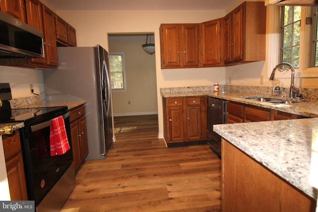 kitchen with light hardwood / wood-style floors, light stone countertops, sink, and appliances with stainless steel finishes