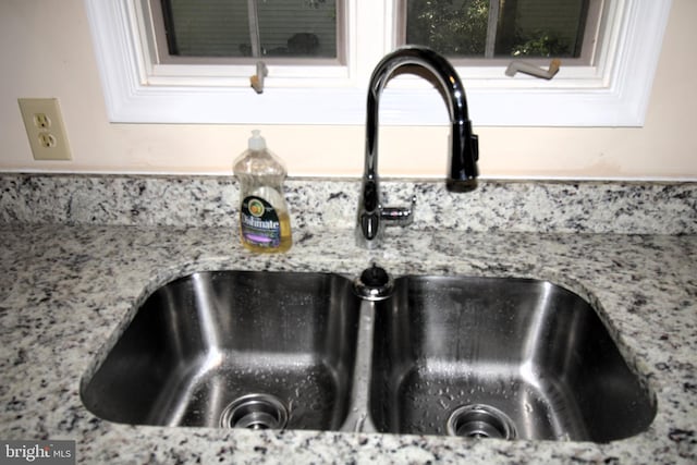 interior details featuring white cabinets, light stone countertops, and sink