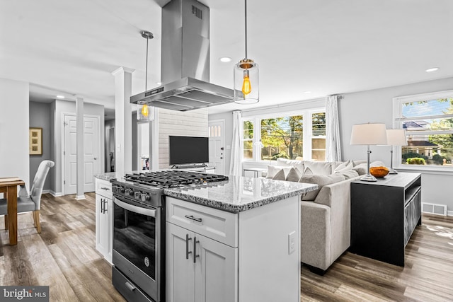 kitchen with a kitchen island, wall chimney exhaust hood, pendant lighting, and stainless steel range with gas cooktop