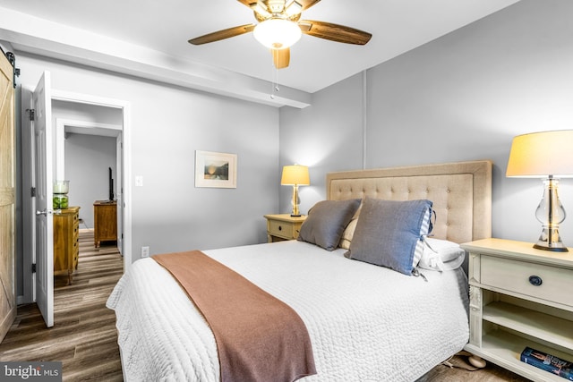 bedroom with ceiling fan, a barn door, and dark hardwood / wood-style floors