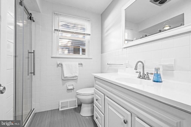 bathroom with vanity, toilet, tile walls, tile patterned flooring, and a shower with door