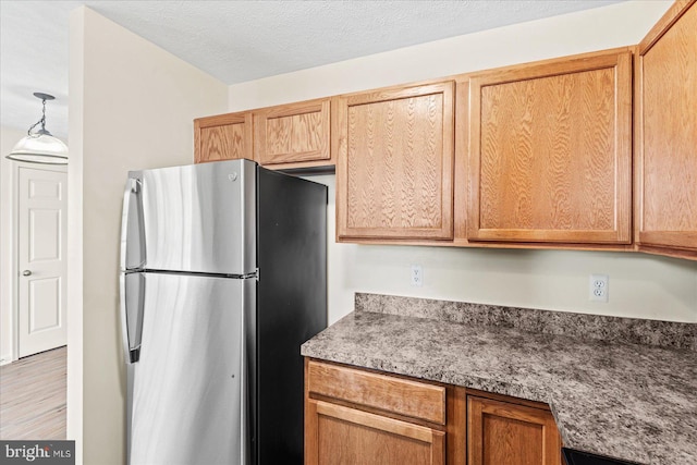 kitchen featuring a textured ceiling, stainless steel refrigerator, and hanging light fixtures