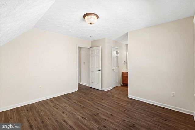 unfurnished bedroom with lofted ceiling, dark hardwood / wood-style flooring, and a textured ceiling