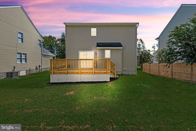 back house at dusk with a yard, a wooden deck, and central AC