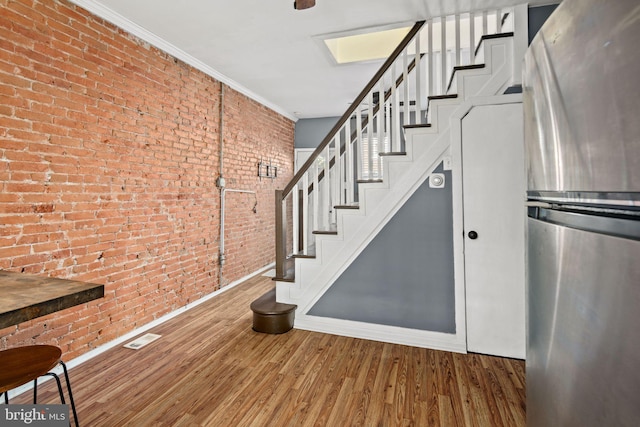 stairway with wood-type flooring, crown molding, and brick wall