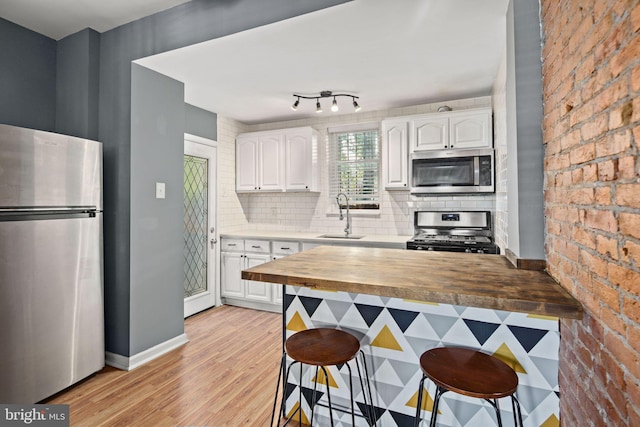 kitchen featuring wooden counters, white cabinets, sink, appliances with stainless steel finishes, and a kitchen bar