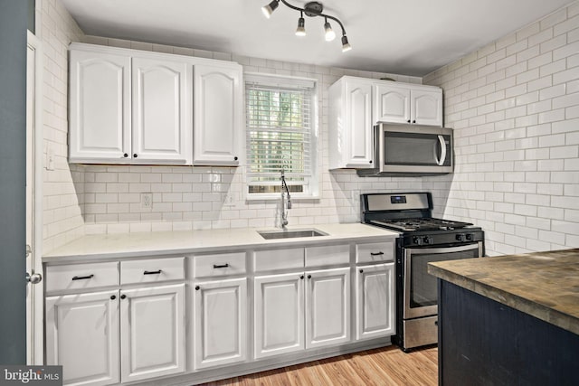 kitchen with white cabinets, sink, decorative backsplash, appliances with stainless steel finishes, and light hardwood / wood-style floors