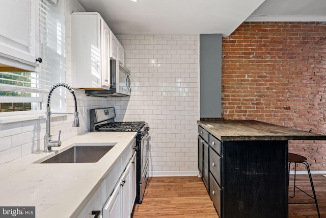 kitchen with sink, light wood-type flooring, appliances with stainless steel finishes, white cabinetry, and a breakfast bar area