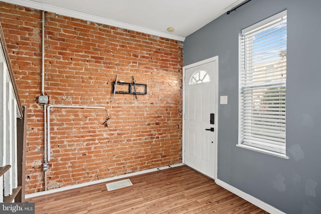 foyer entrance featuring crown molding, brick wall, and hardwood / wood-style flooring