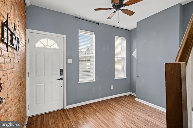 foyer with ceiling fan, light hardwood / wood-style floors, and brick wall