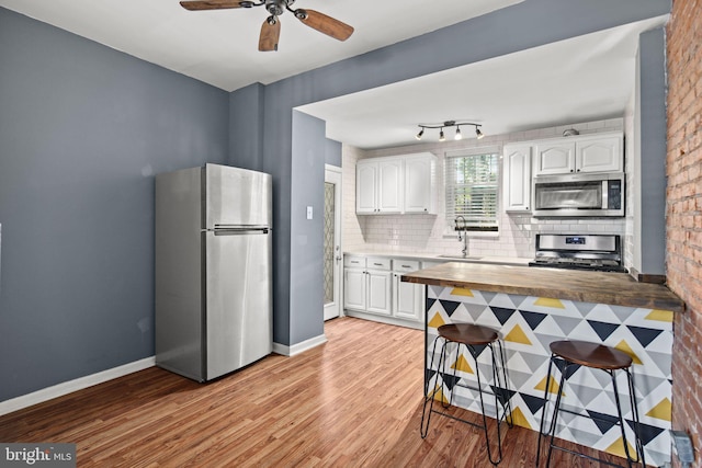 kitchen featuring butcher block counters, stainless steel appliances, brick wall, white cabinets, and light wood-type flooring