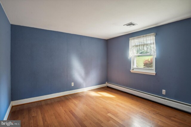 empty room featuring hardwood / wood-style flooring and a baseboard radiator