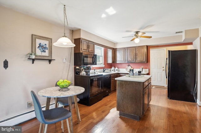 kitchen with wood-type flooring, dark brown cabinets, decorative light fixtures, a center island, and black appliances