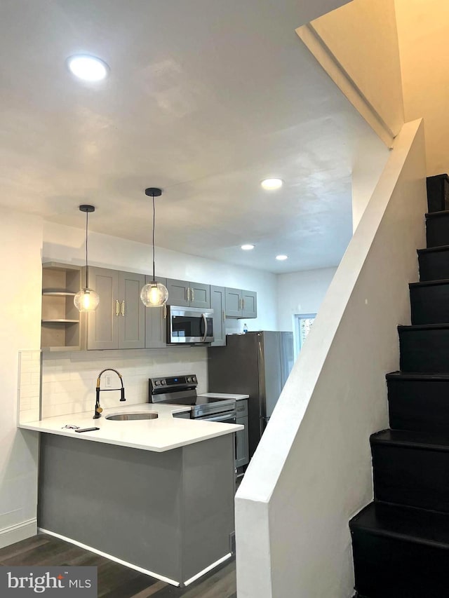 kitchen with sink, stainless steel appliances, dark wood-type flooring, kitchen peninsula, and pendant lighting