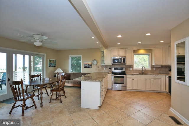 kitchen featuring appliances with stainless steel finishes, kitchen peninsula, light stone counters, and a healthy amount of sunlight