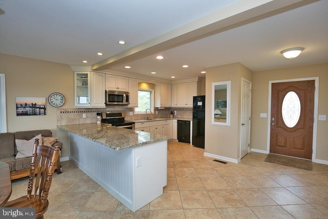 kitchen with kitchen peninsula, black appliances, decorative backsplash, and light stone countertops